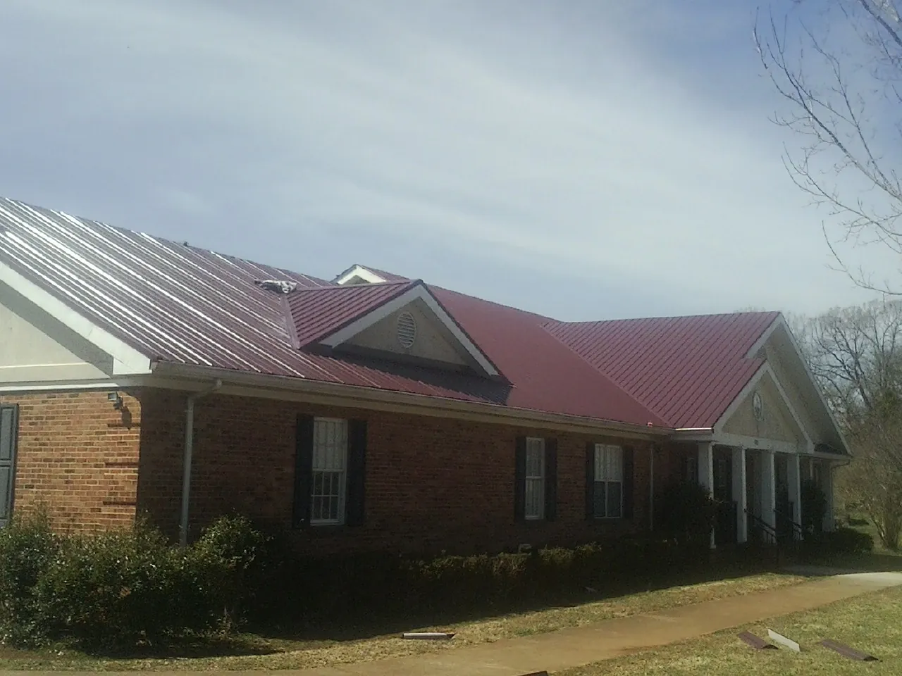 Red metal roof with gabled entries on a long brick building, from a Hail Damage Roof Repair job in Robstown