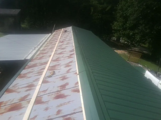 Old rusted panels beside newly installed green metal roofing — Wind Damage Roof Repair by Roofing Brothers in Robstown