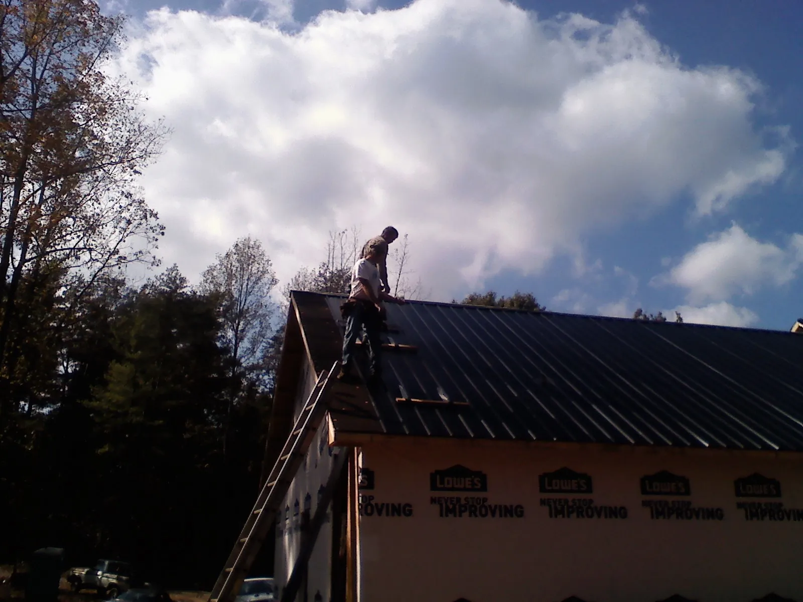 Roofer fastening dark metal panels high against a cloudy sky, from a Roof Inspection job in Robstown