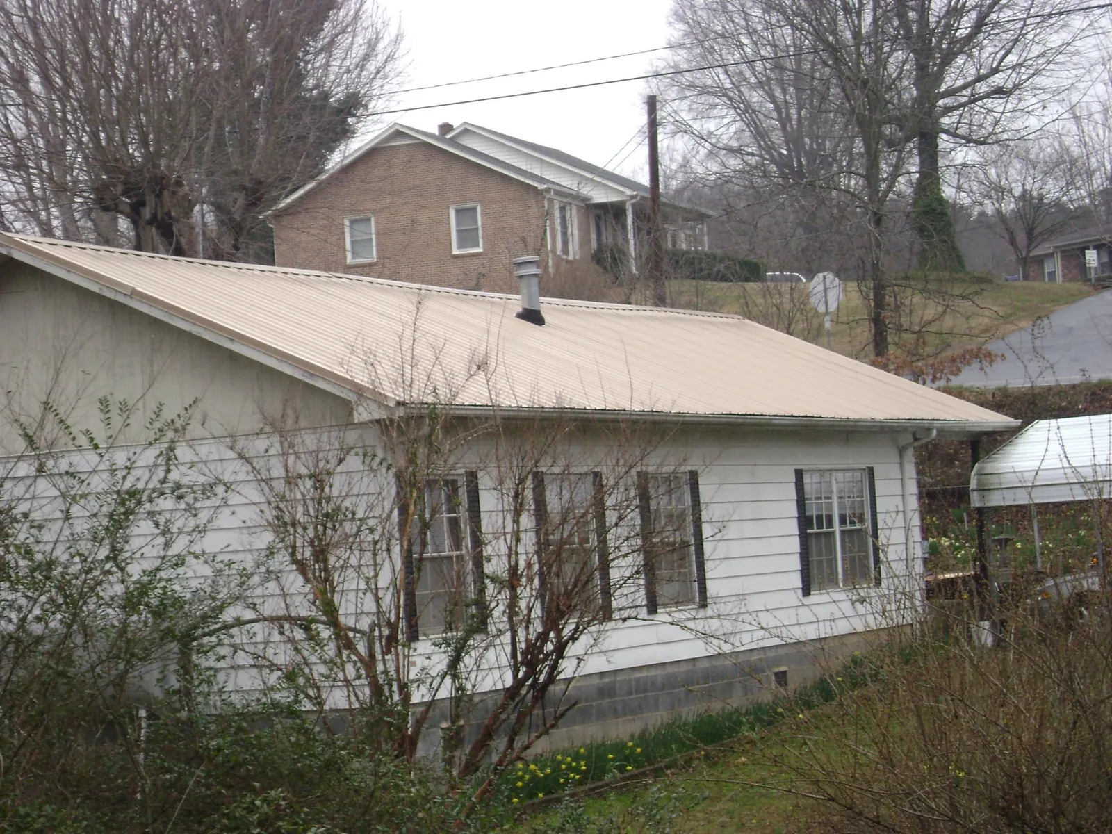 Tan metal roof on a white sided house set into a hillside — Commercial Roofing by Roofing Brothers in Robstown